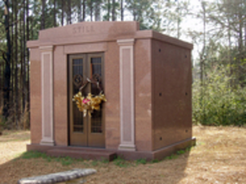 Tall red stone mausoleum with carved pillars on each side and one metal door